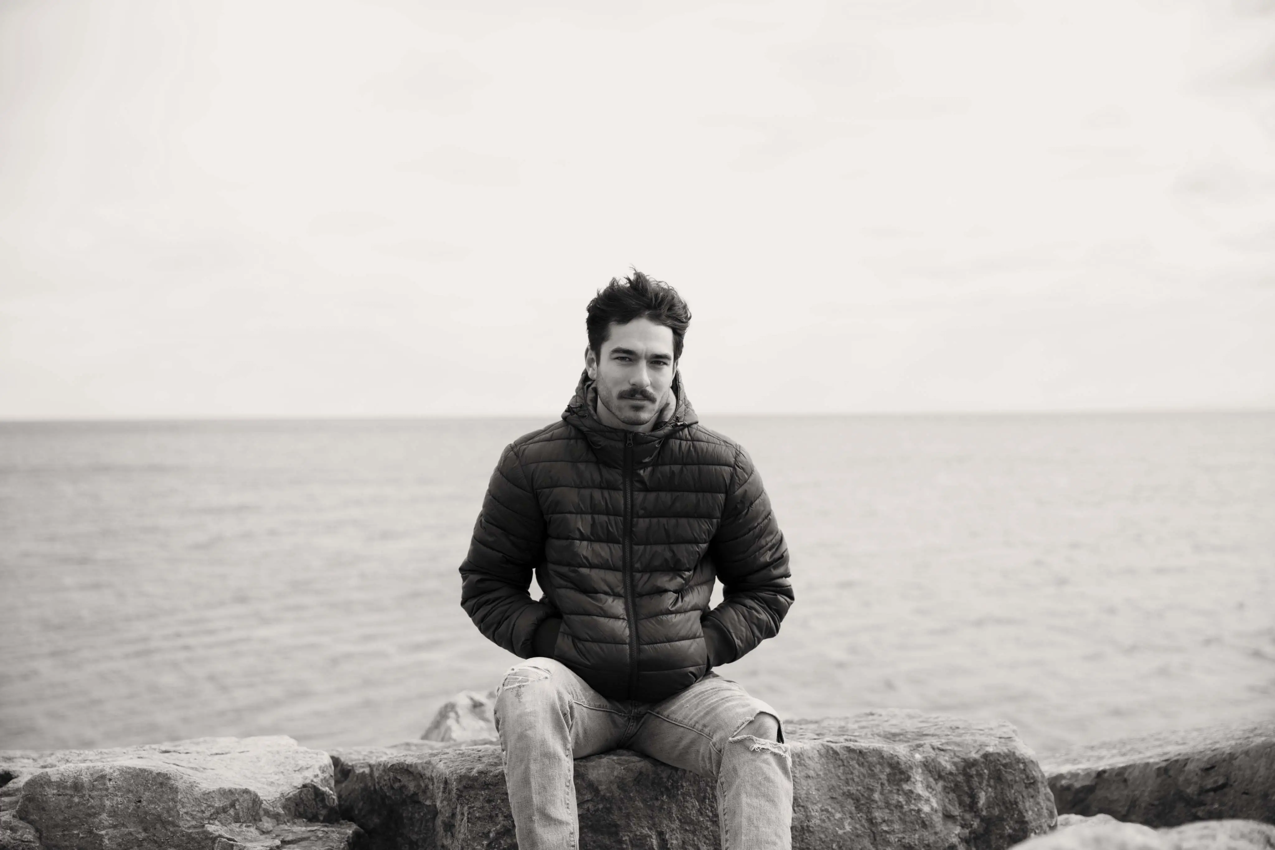 Young man sitting on a rock with his back to the sea